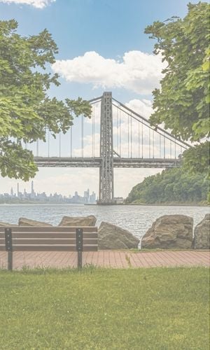 View of the George Washington Bridge over the Hudson River, framed by trees in Upper Manhattan during daylight.