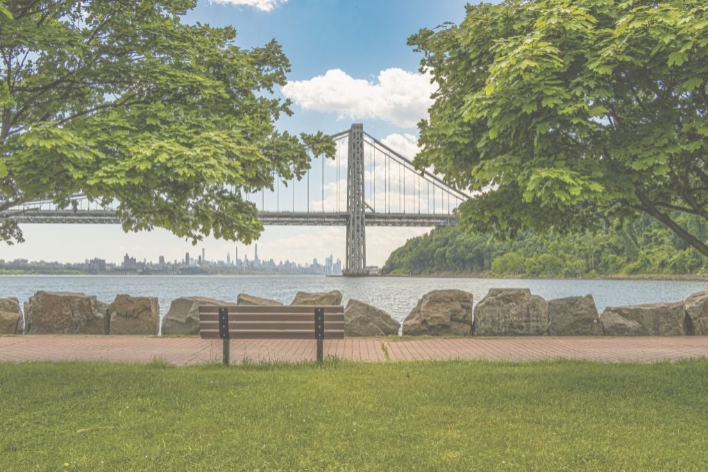 Upper Manhattan view of the George Washington over the Hudson River, framed by trees in daylight.