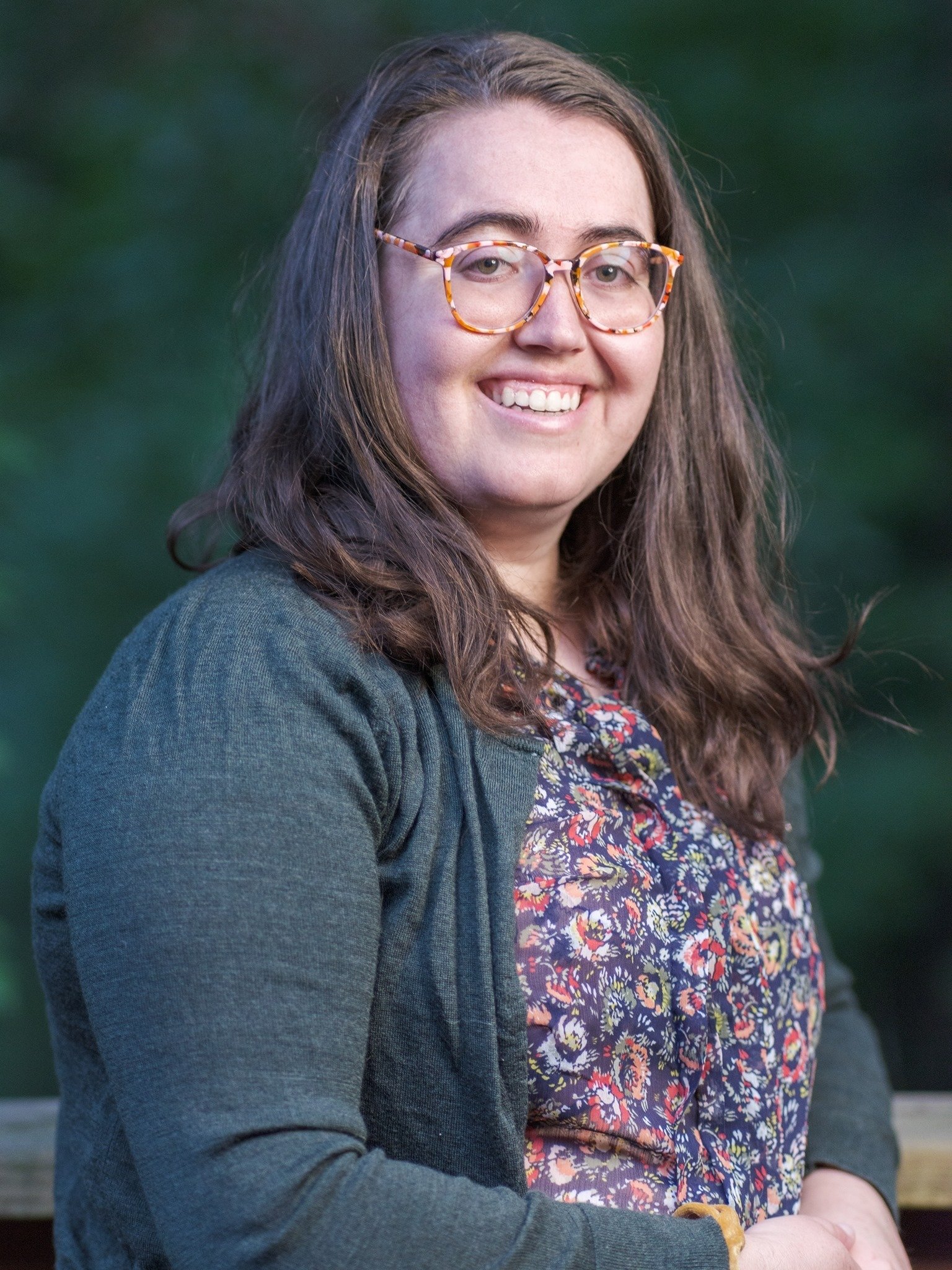 Emma, a white woman with long brown hair, colorful glasses, is similing