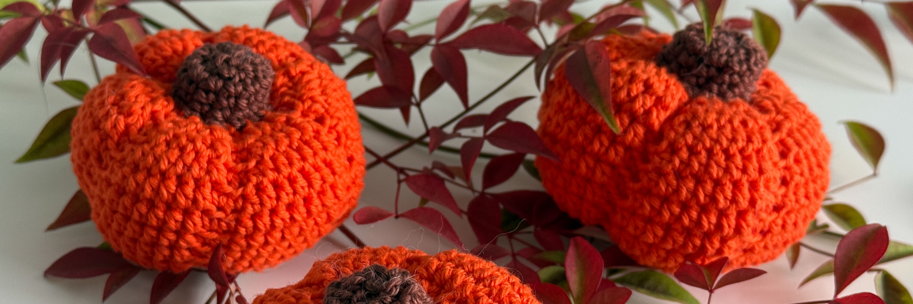 Two small orange crochet pumpkins are nestled amongst autumn foliage.