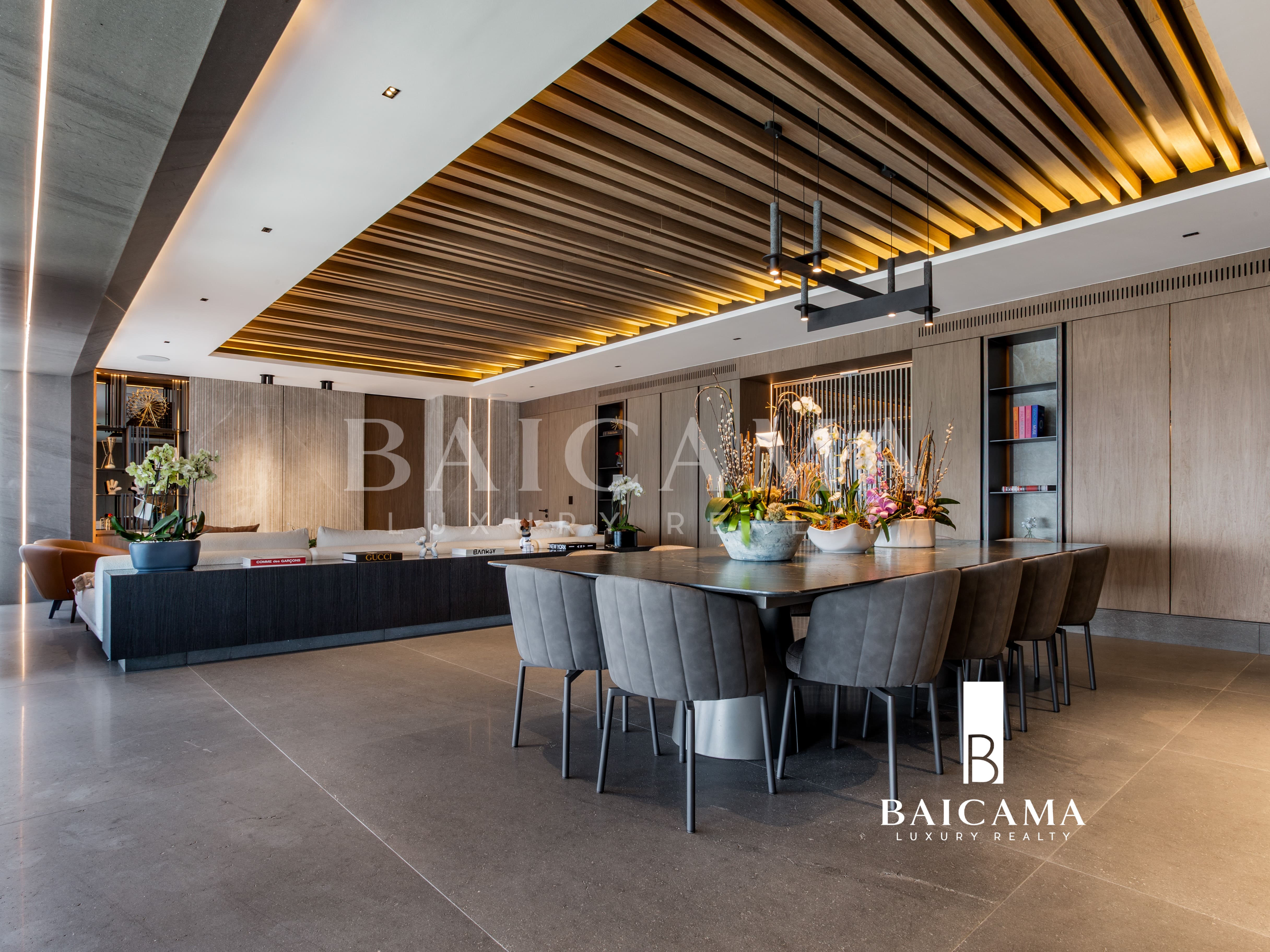 Departamento de Lujo en Residence, Bosque Real. CDMX. Comedor de lujo con diseño contemporáneo, mesa de gran formato, sillas tapizadas en tonos neutros, plafón de madera con iluminación indirecta, cocina abierta de alta gama y acabados sofisticados que crean un ambiente elegante y funcional.