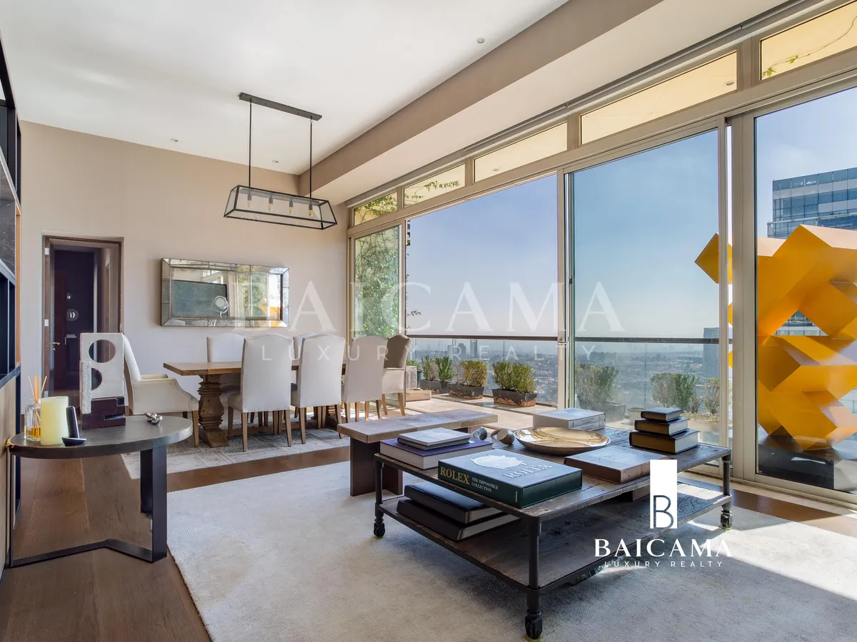 Sala de estar moderna en departamento de lujo en Club Residencial Bosques, con muros de acabado gris, librero de diseño en madera y metal, arte contemporáneo, mesa de centro con libros y detalles decorativos.