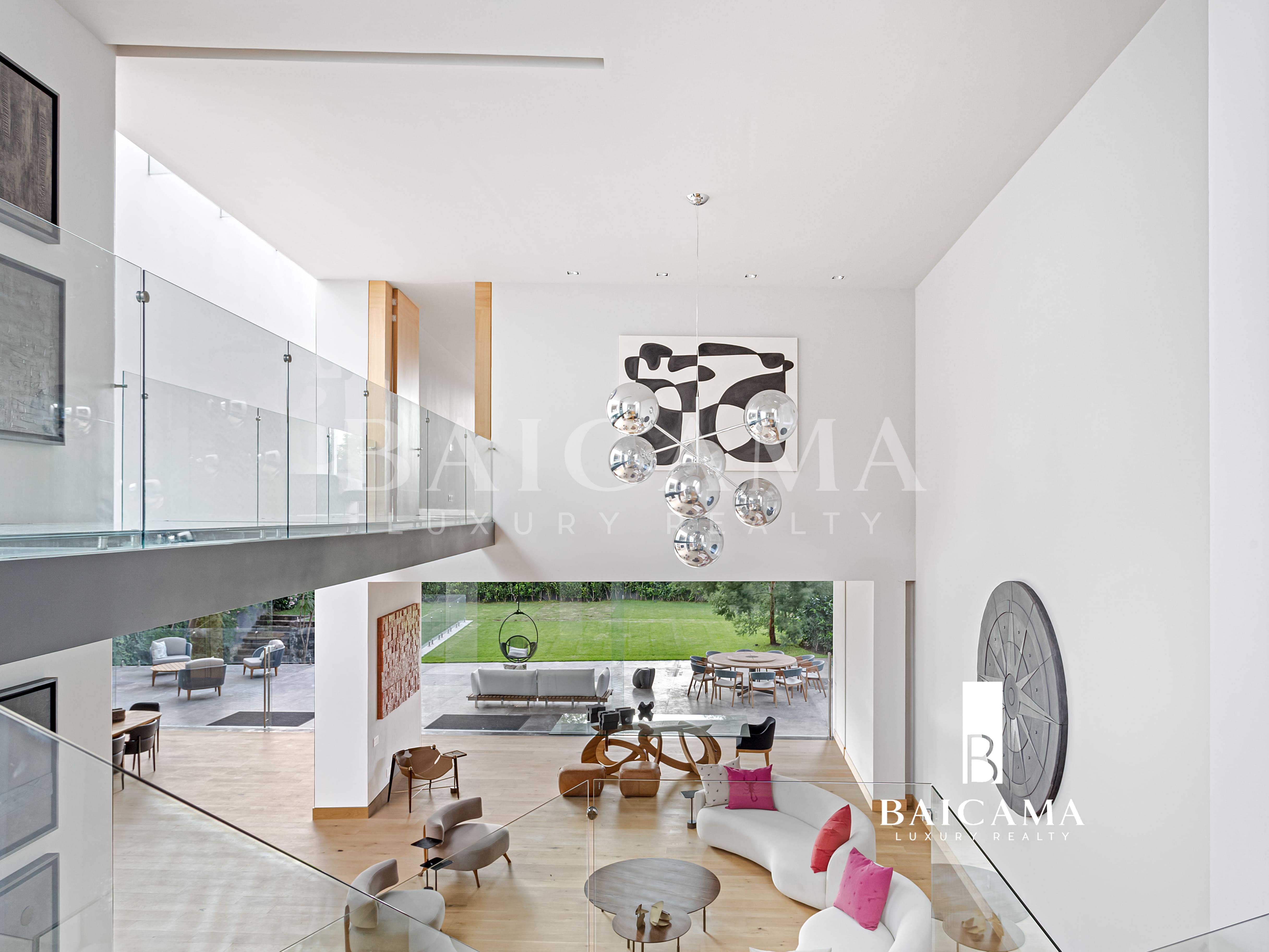 Casa de Lujo en Jardines del Pedregal 100 millones de pesos CDMX. Sala de doble altura en residencia de lujo con diseño contemporáneo, barandales de cristal, luminaria escultórica, mobiliario moderno en tonos neutros, grandes ventanales y vista directa al jardín, integrando interior y exterior con abundante luz natural.