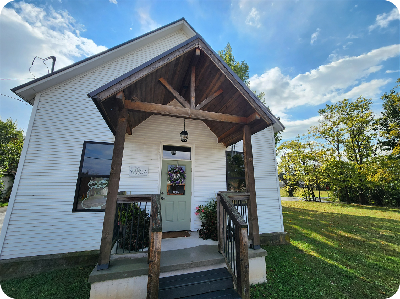 Exterior of And Now, Yoga where Gentle Balance is located. The black and white and dark wood building pops out on a sunny day with blue skies and green grass