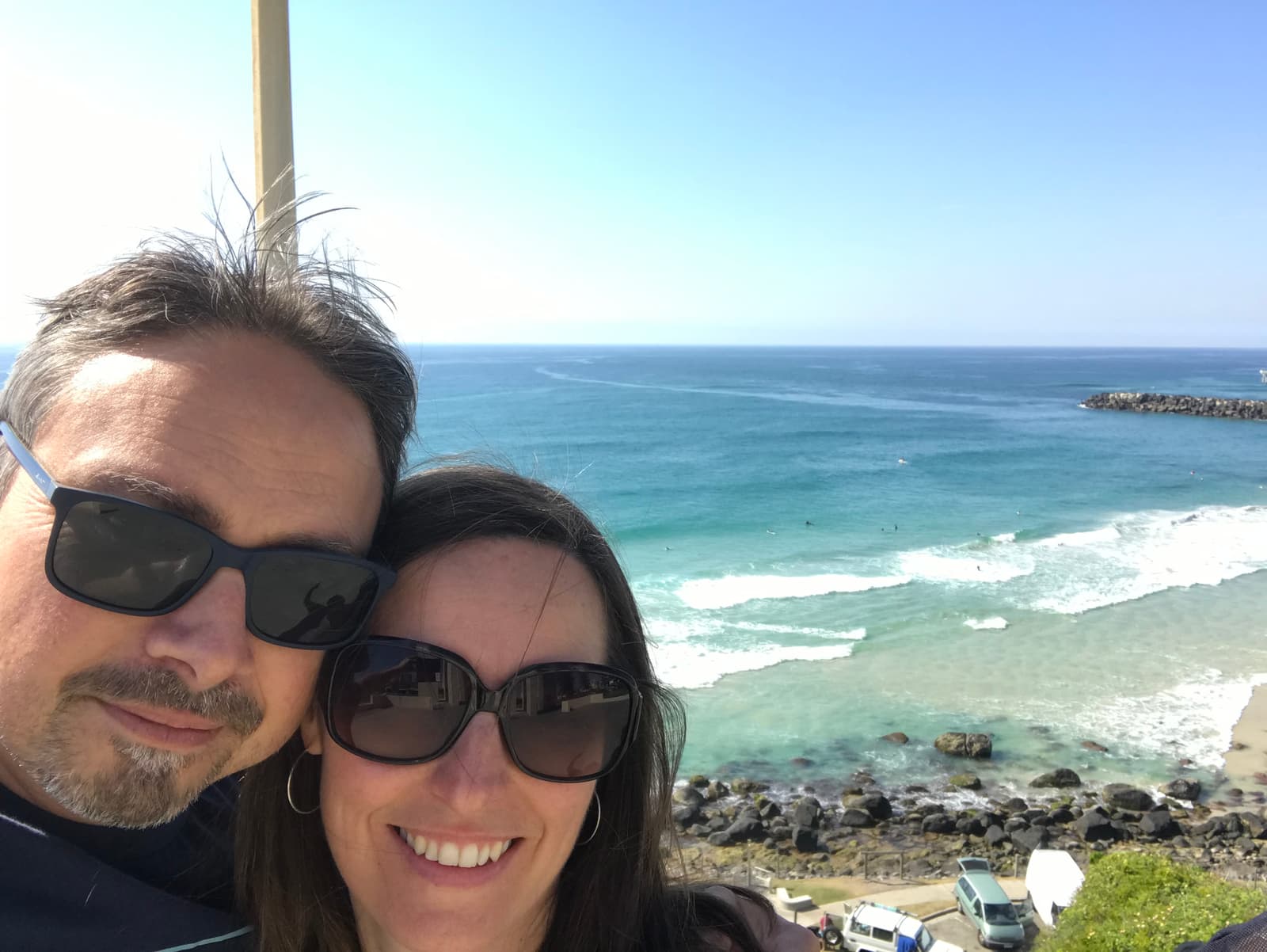 Kim and Greg, founders of Andersons Eco Retreat, on a hill overlooking the ocean on a sunny day.