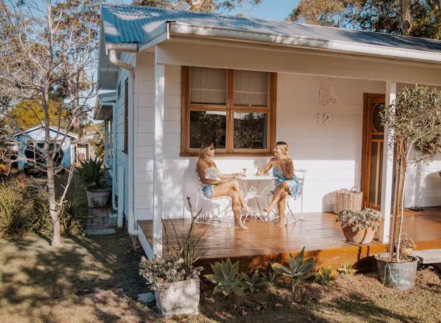 Two women relaxing on a sunny veranda, sipping wine at a cabin retreat