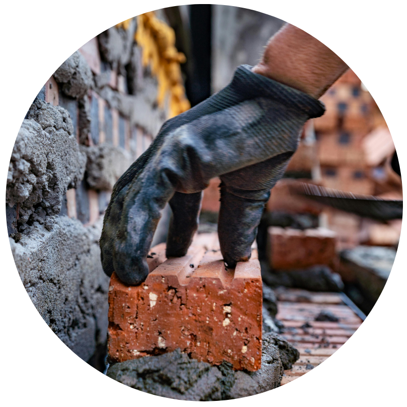 gloved hand holding a brick with mortar
