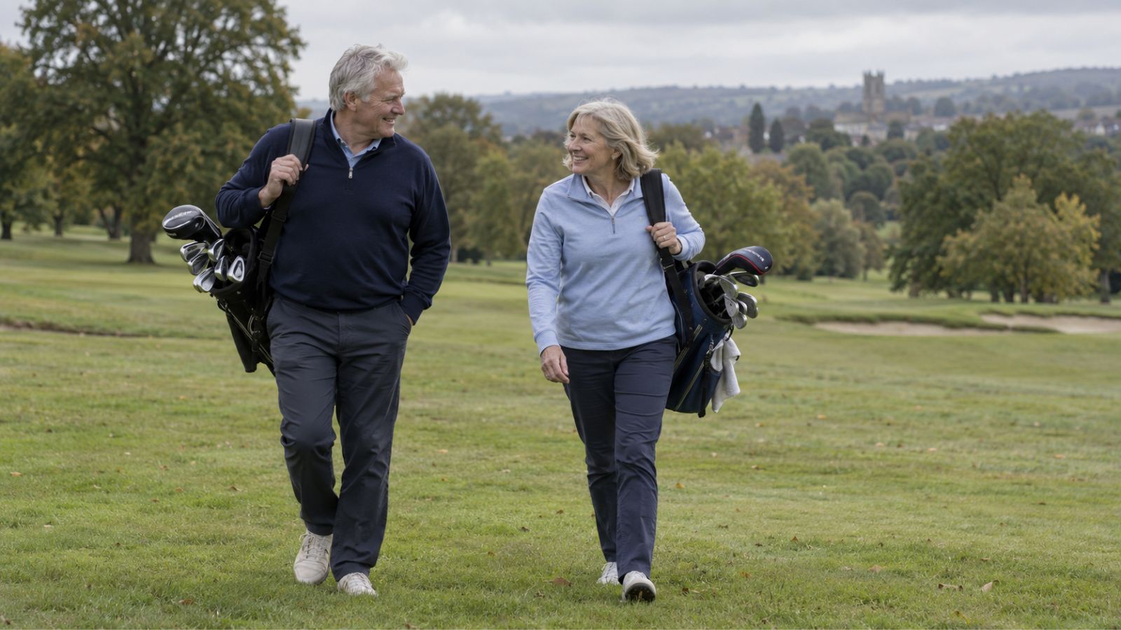 Older man and woman golfers walking across a golf course carrying their bags