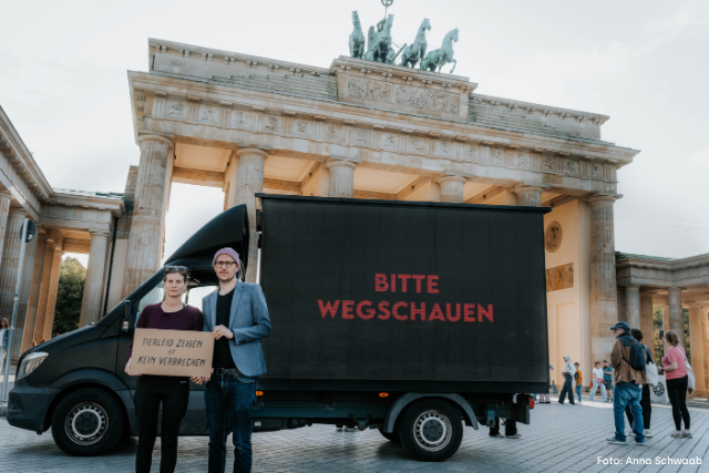 Anna und Hendrik stehen vor dem Brandenburger Tor mit dem Video-LKW und einem Schild in den Händen: