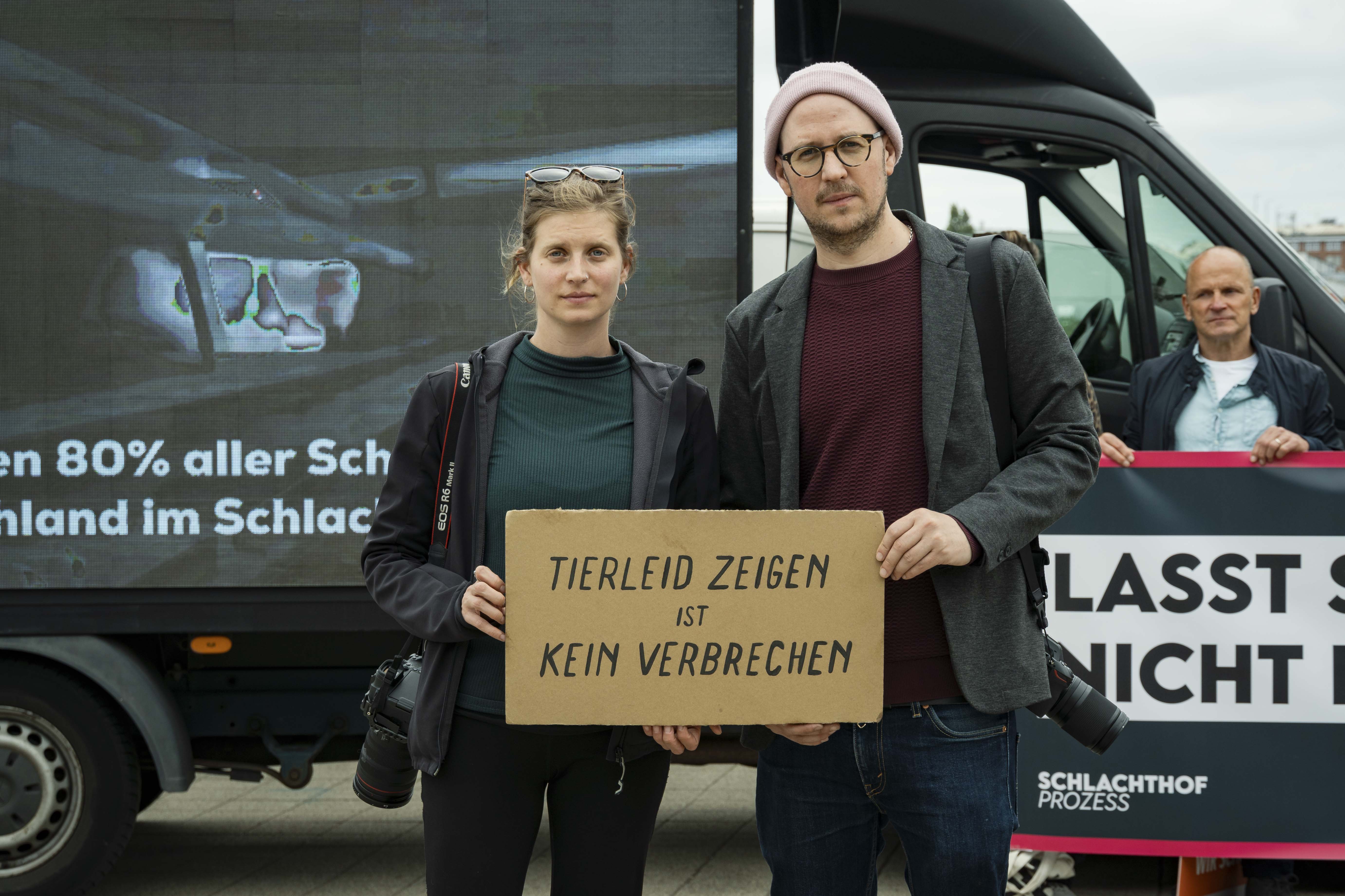 Anna und Hendrik stehen vor dem Brandenburger Tor mit dem Video-LKW und einem Schild in den Händen:
