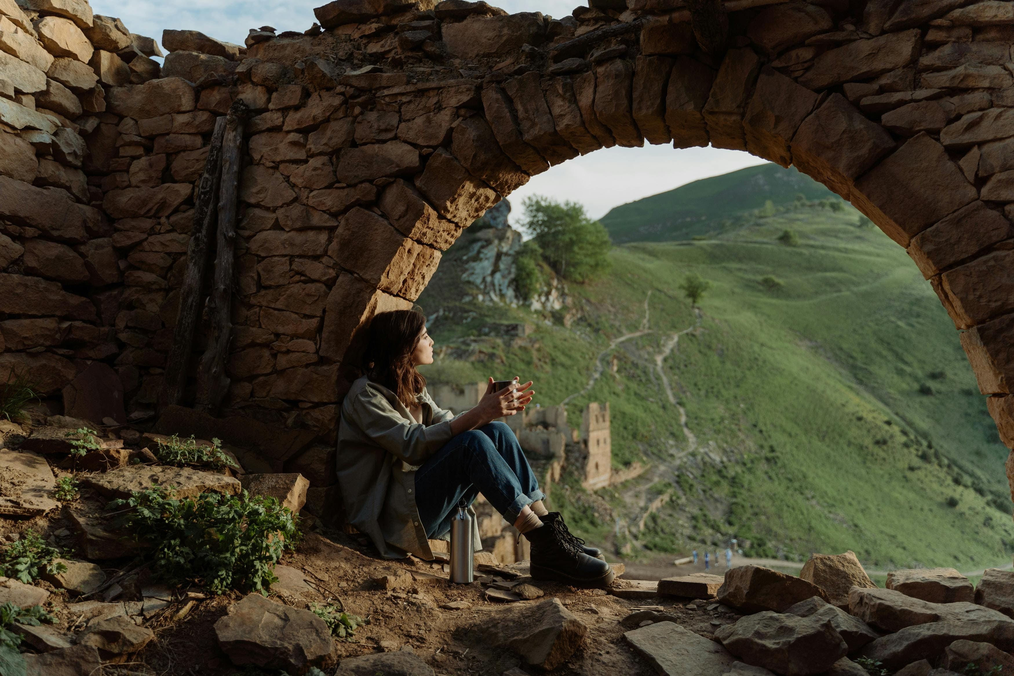 Woman sitting by stone circle contemplating landscape view during reflective travel transformation coaching