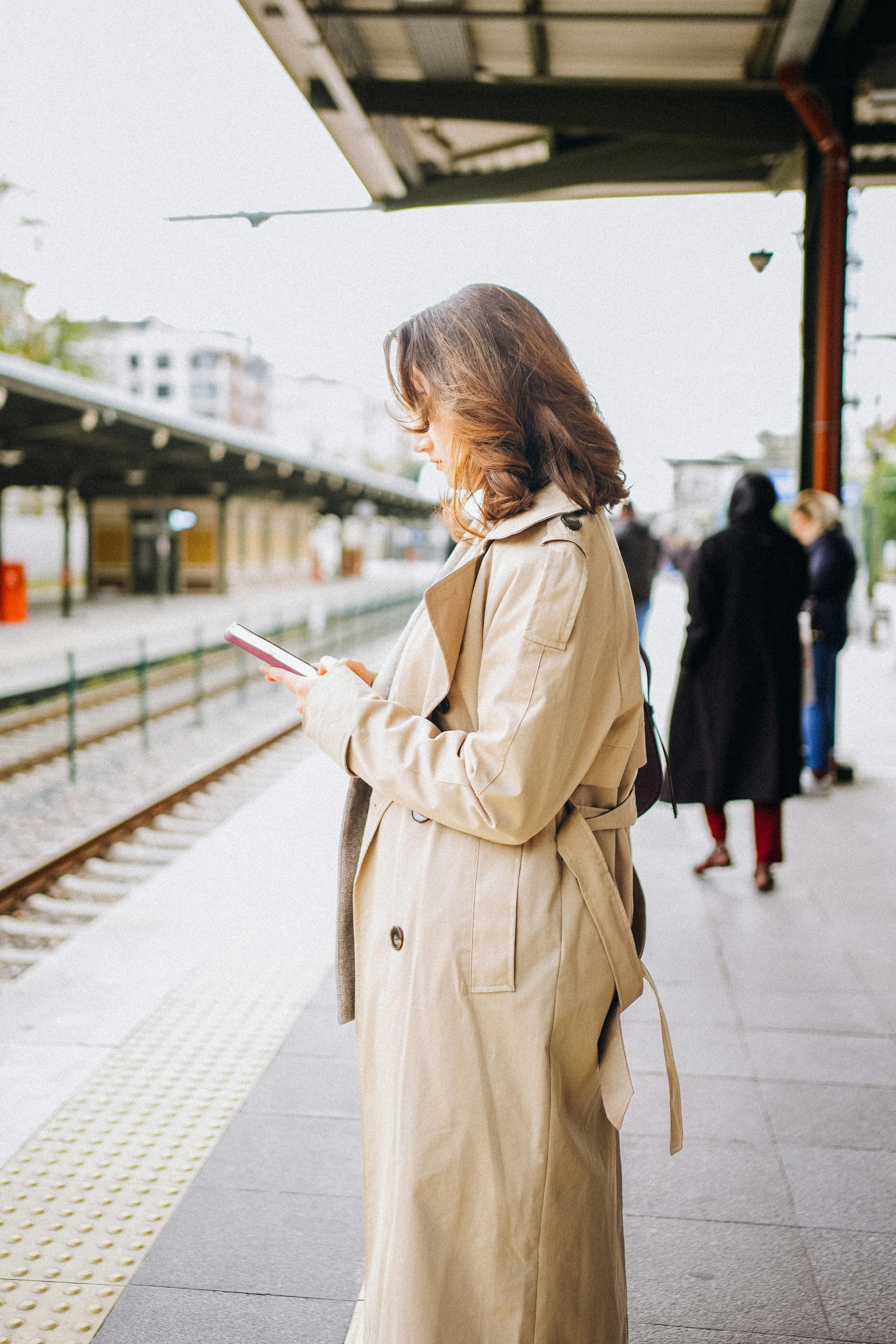 Woman checking phone at train station during travel coaching support, staying connected while journeying