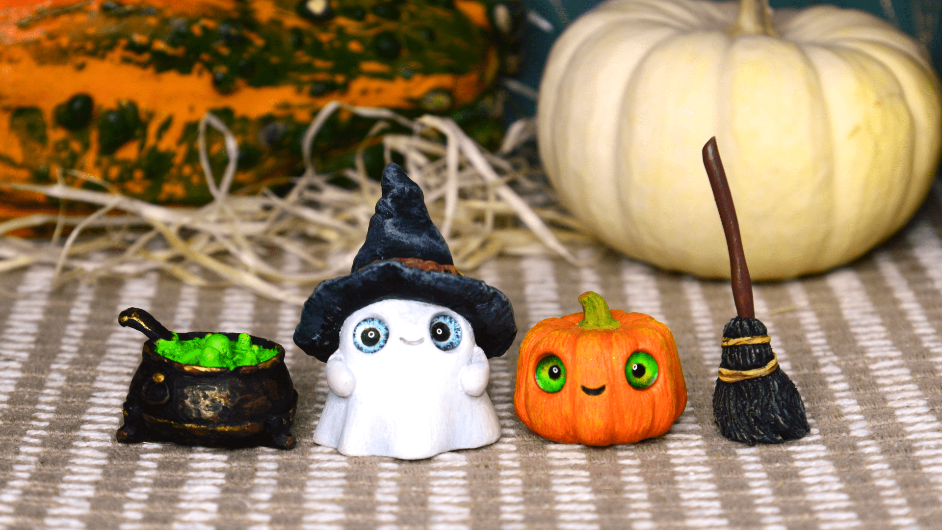 Figures of a ghost in a hat, mini pumpkins, a cauldron with a potion, and a broom against a background of pumpkins
