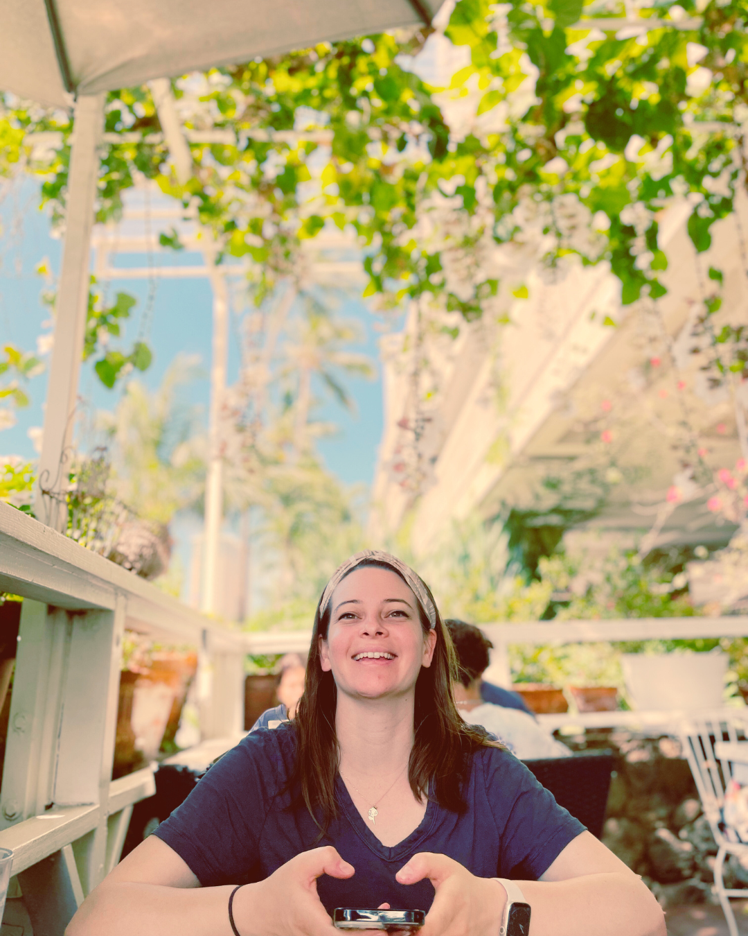 Picture of Brittany smiling while holding a phone and wearing a blue t-shirt on a patio