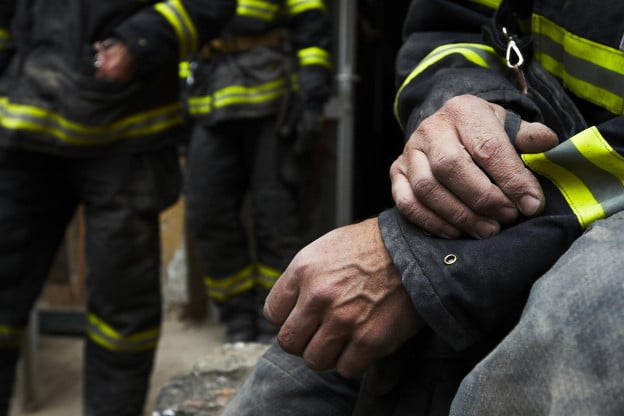 A firefighter's hands, zoomed in where the face is not pictured, crossed over each other while the firefighter is in gear.