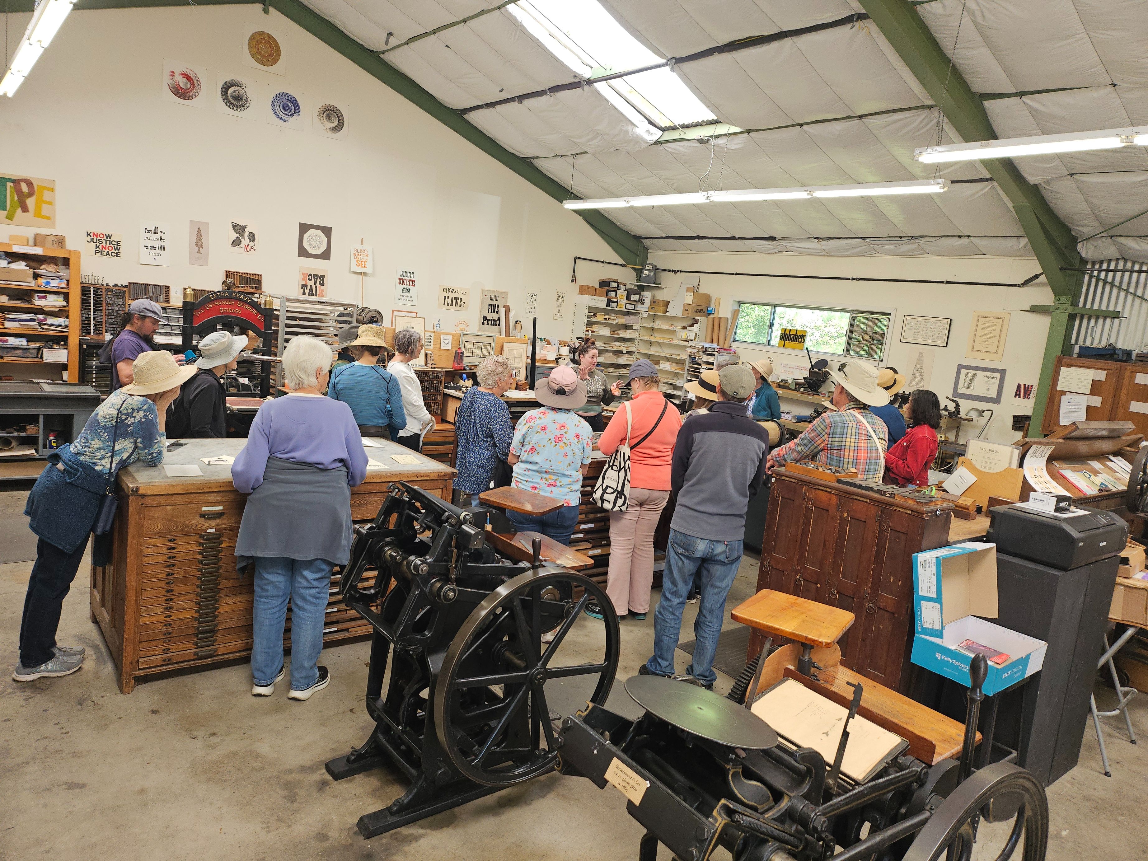 Walkers gathered around vintage presses in a letterpress print shop.
