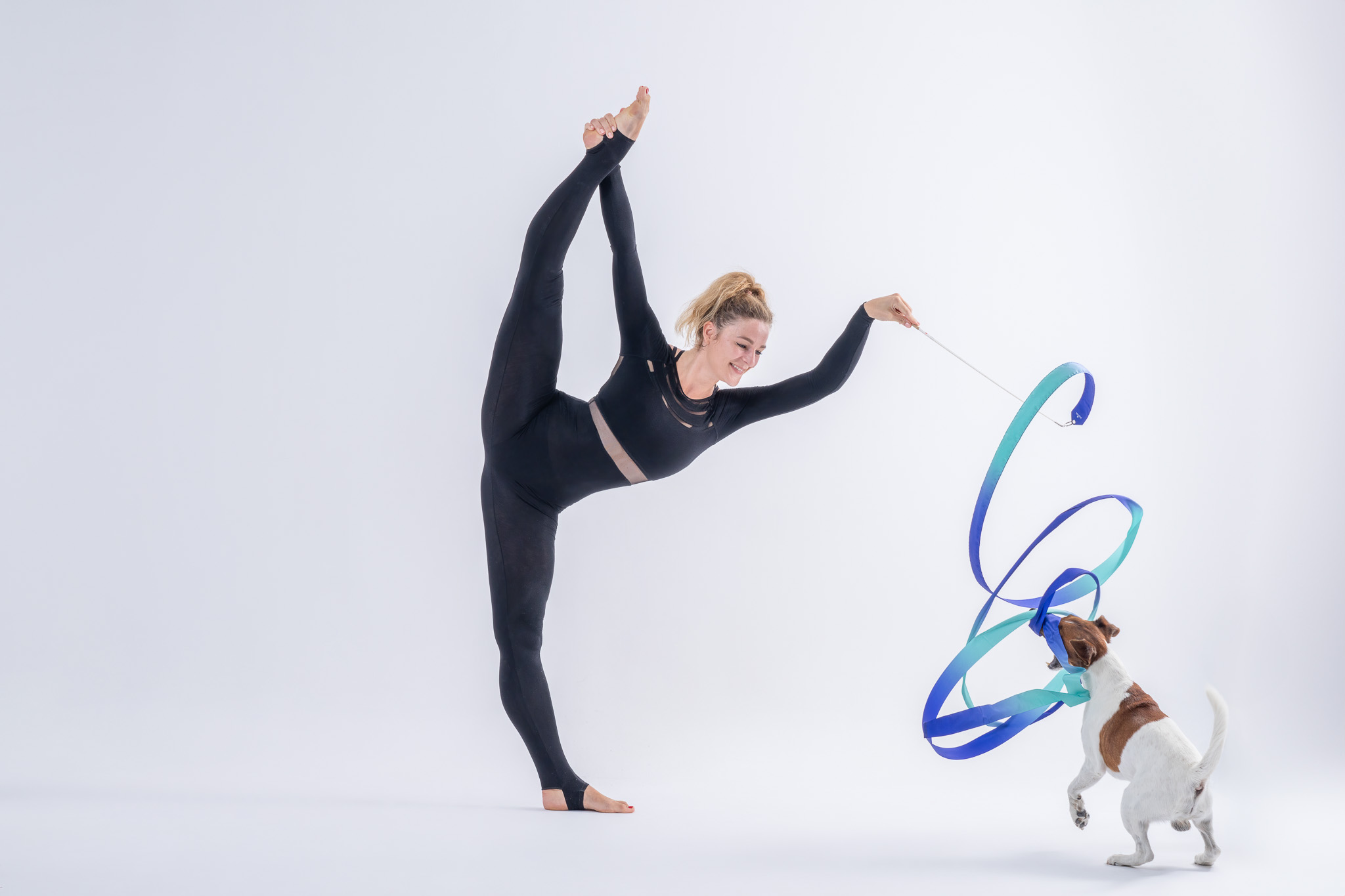 tancerka w wysokiej pozie równoważnej bawi się wstążką z psem – artystyczna fotografia tańca i psów w studio
