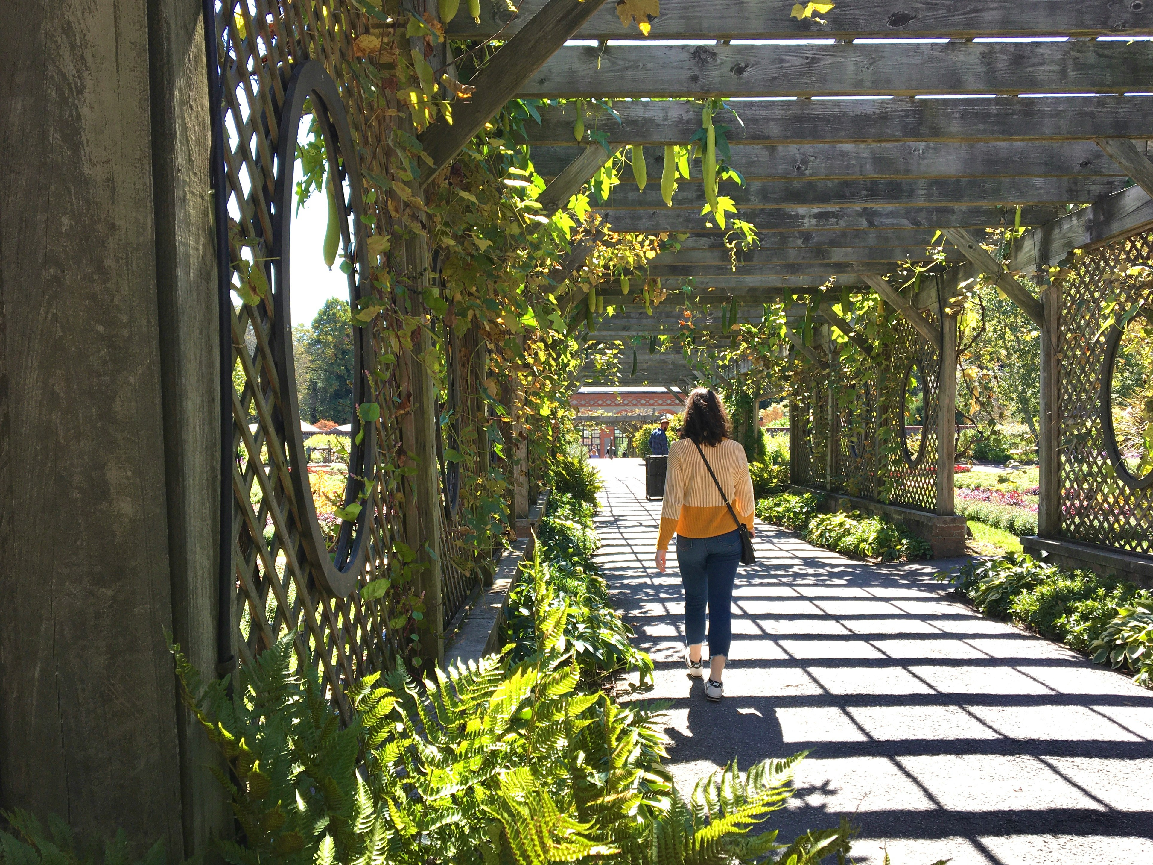 woman walking down a path with lattice walls and greenery in north carolina