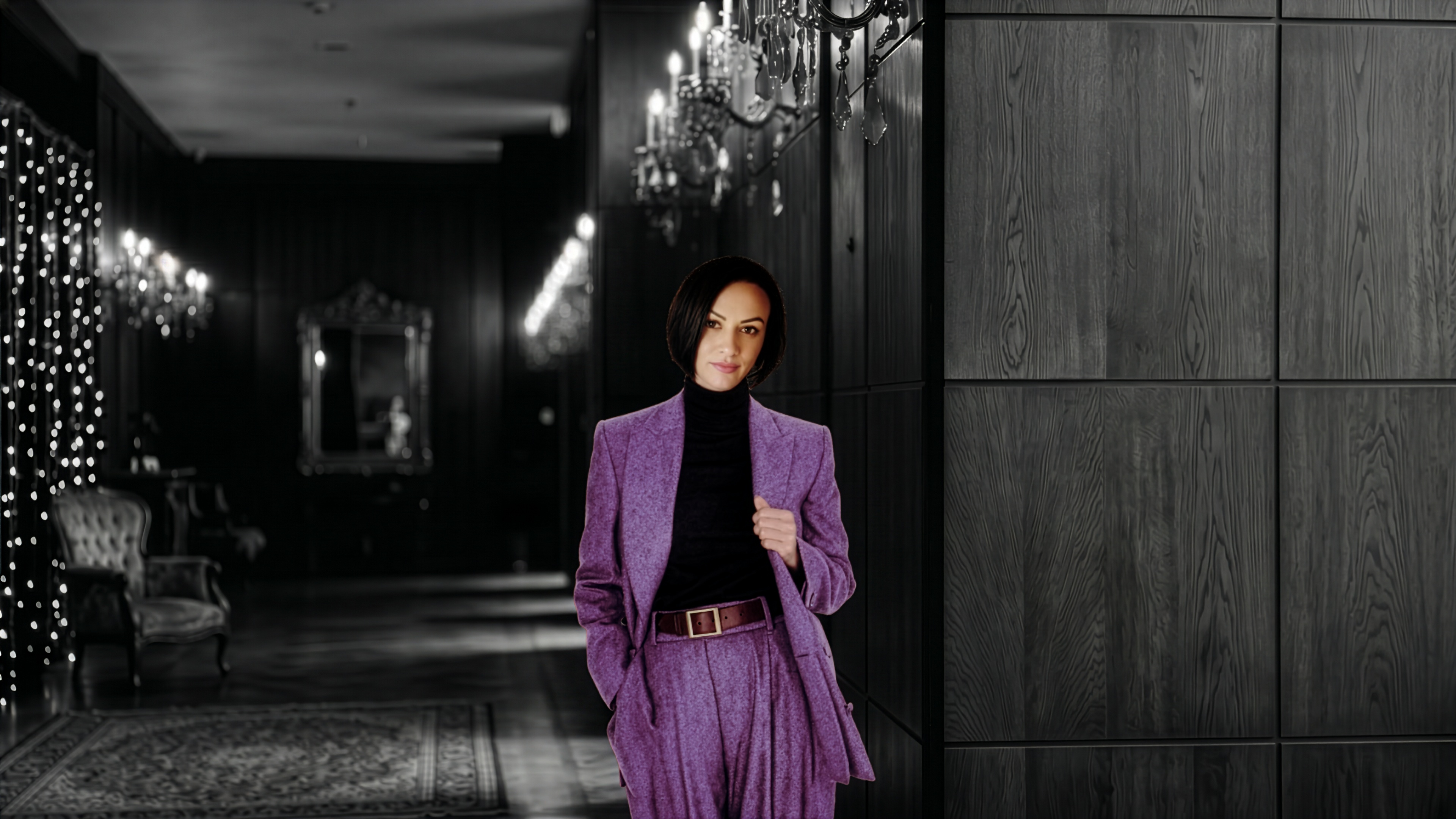 Mirela Bocanet wearing glasses and a blazer, standing in a dimly lit hallway lit by chandeliers, illustrating her journey from human strategy to AI leadership.