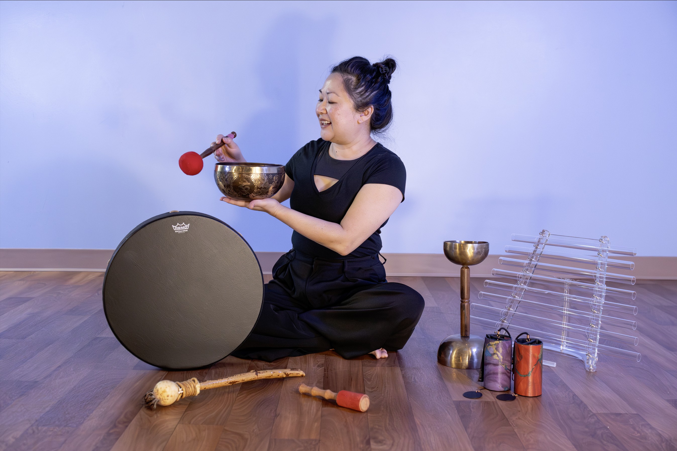 Cinsy Dinges of Harmonic Glowing seated with a professional array of frosted crystal singing bowls and therapeutic sound bath meditation instruments including tibetan bowls, singing bowls, crystal harp