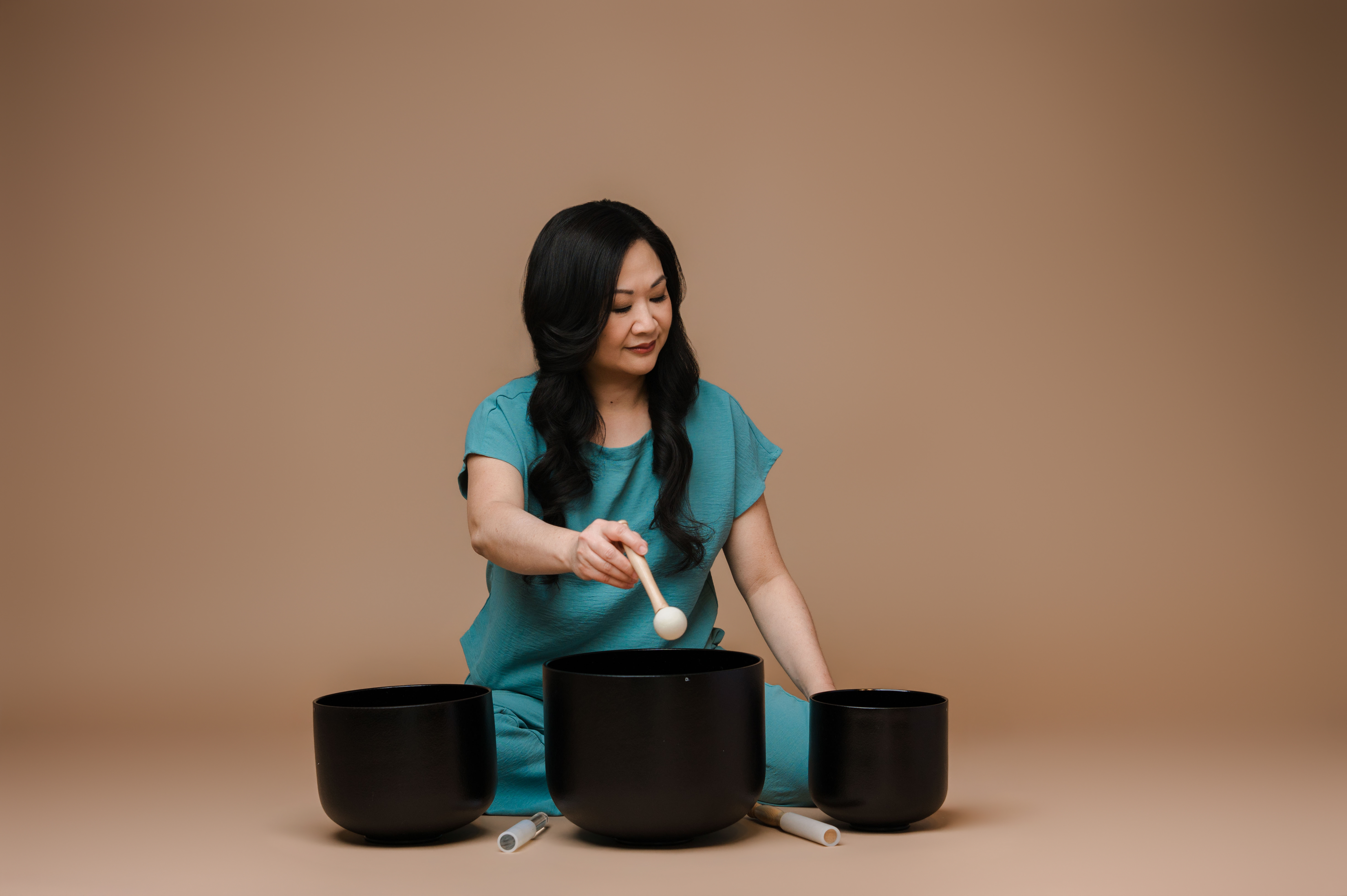Cinsy Dinges of Harmonic Glowing seated with and playing black crystal singing bowls.