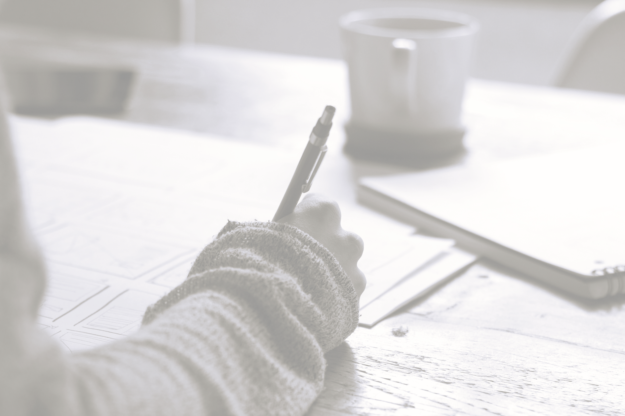 Person writing at a desk with a coffee mug nearby