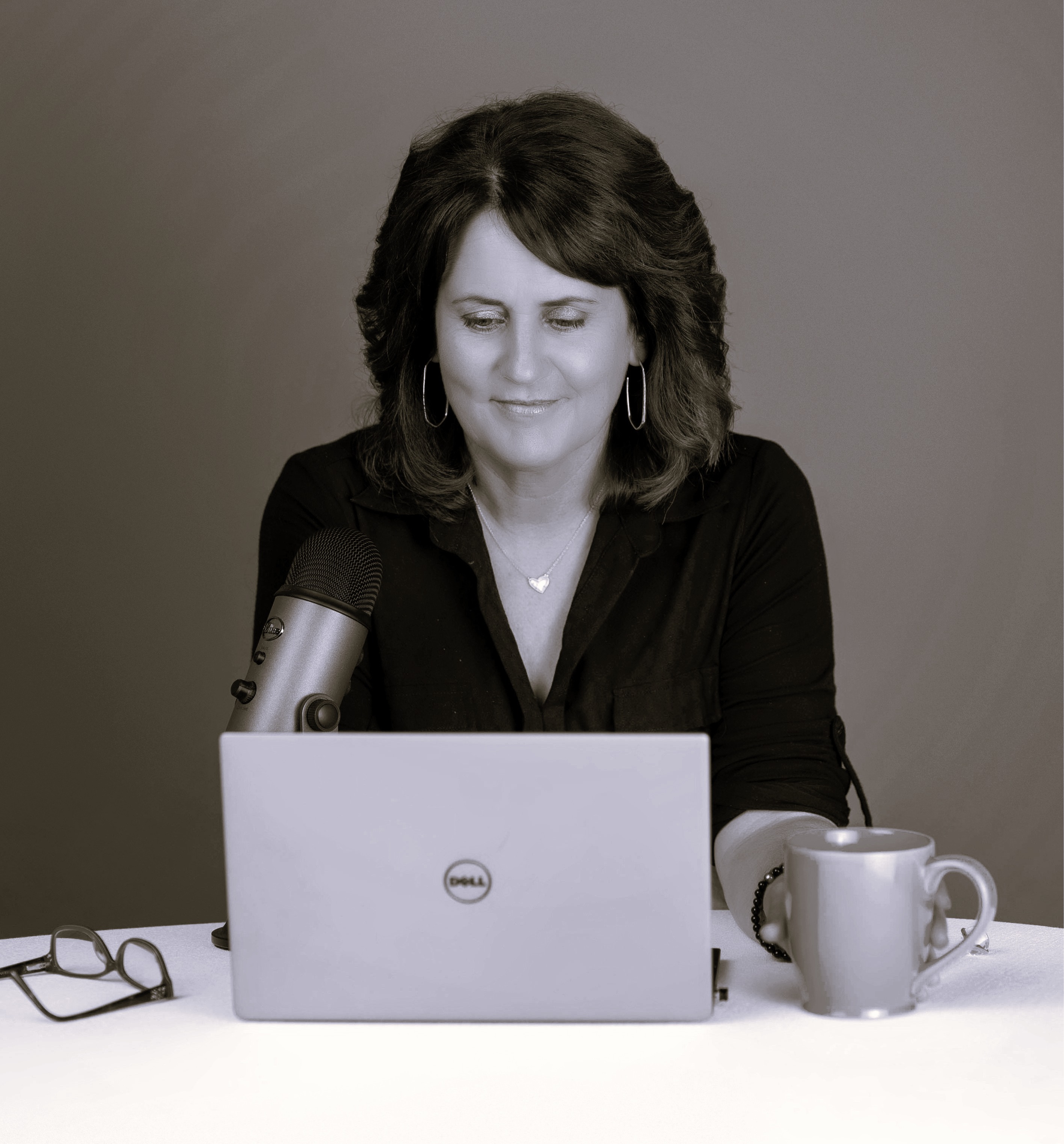 Kimberlee Murray writing at a laptop with a microphone, coffee mug on the table beside her