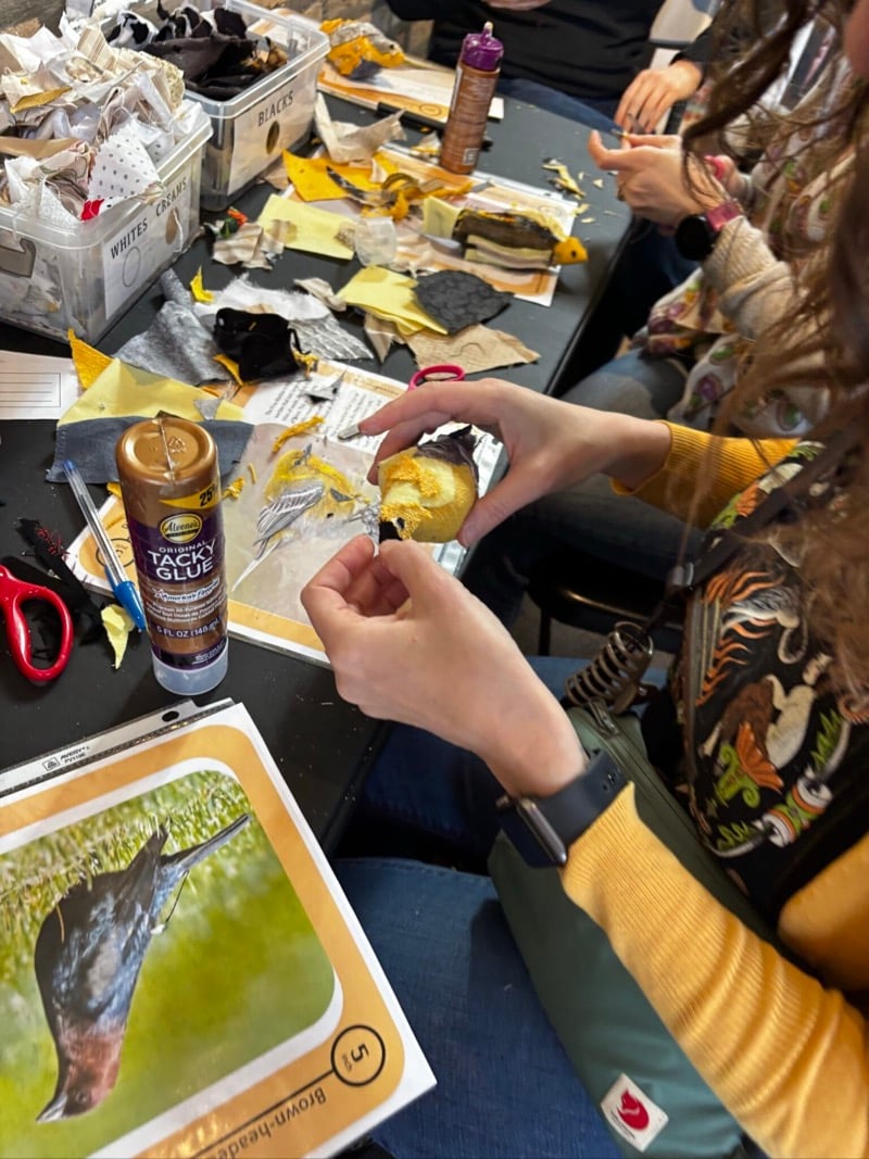 people work around a table making birds from fabric and glue