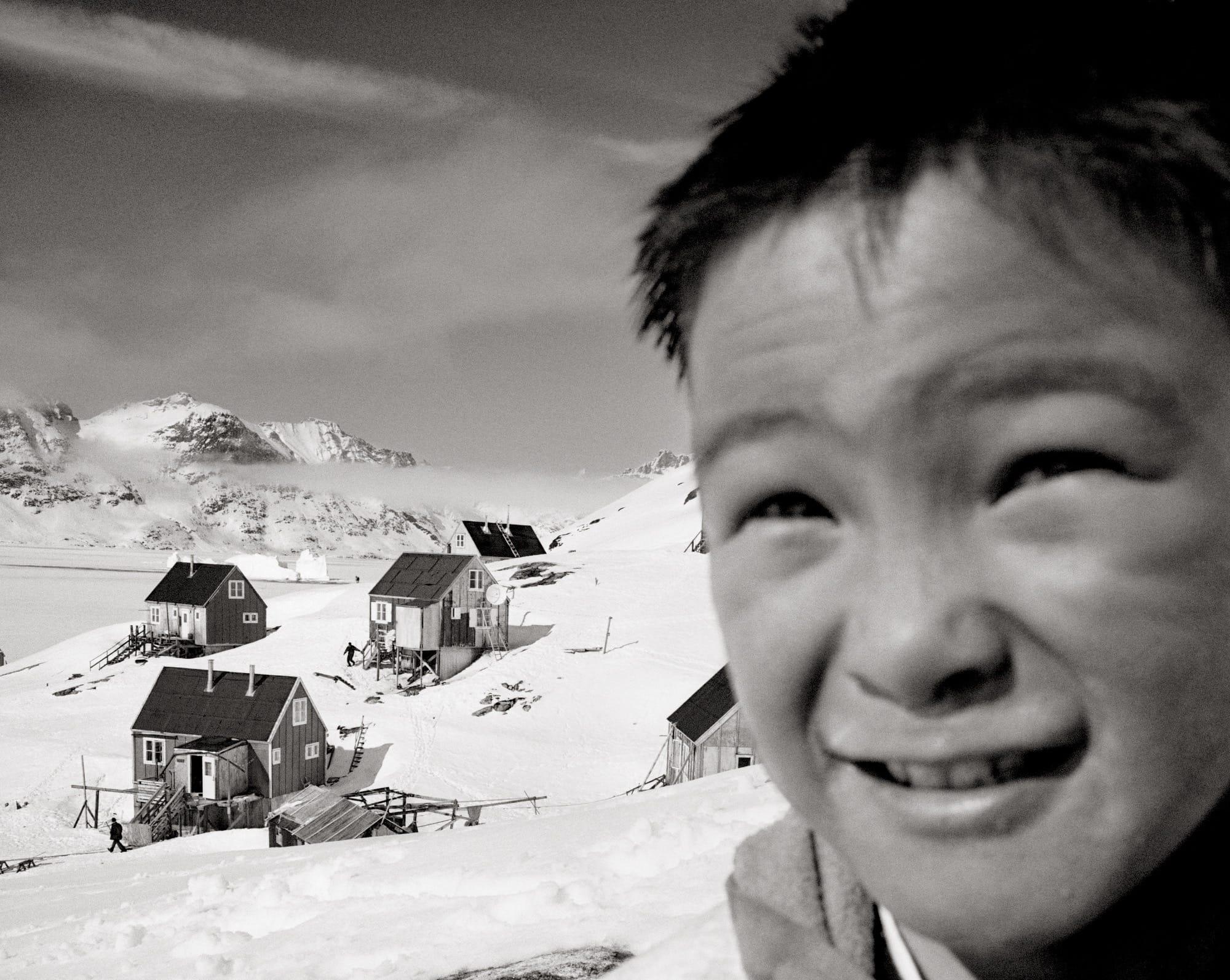 a black and white photo by Ragnar Axelsson of a child in front of a small village