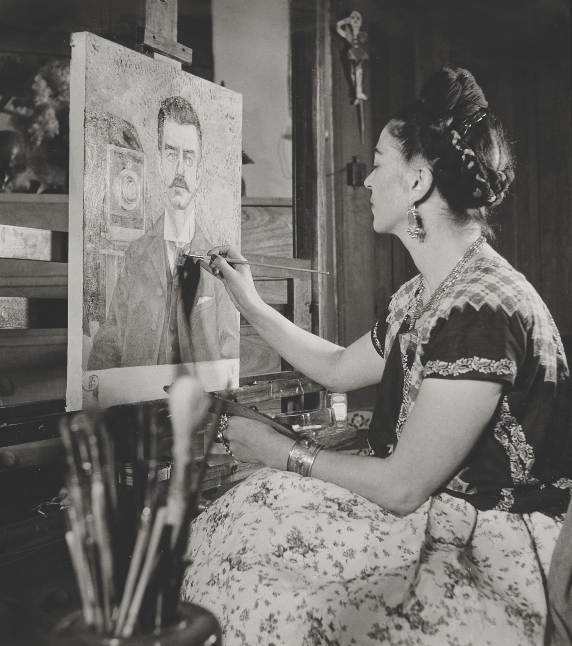 a black and white photo of Frida Kahlo painting a portrait of her father