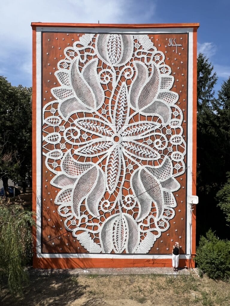 A wall mural on a building in the design of white lace with an orange background by NeSpoon