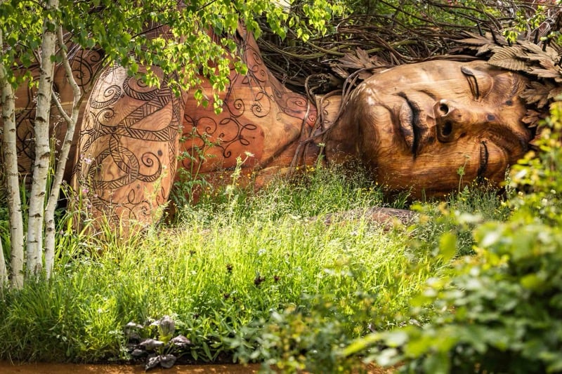 a wooden sculpture of Gaia amid a garden designed by Sarah Eberle at the RHS Chelsea Flower Show