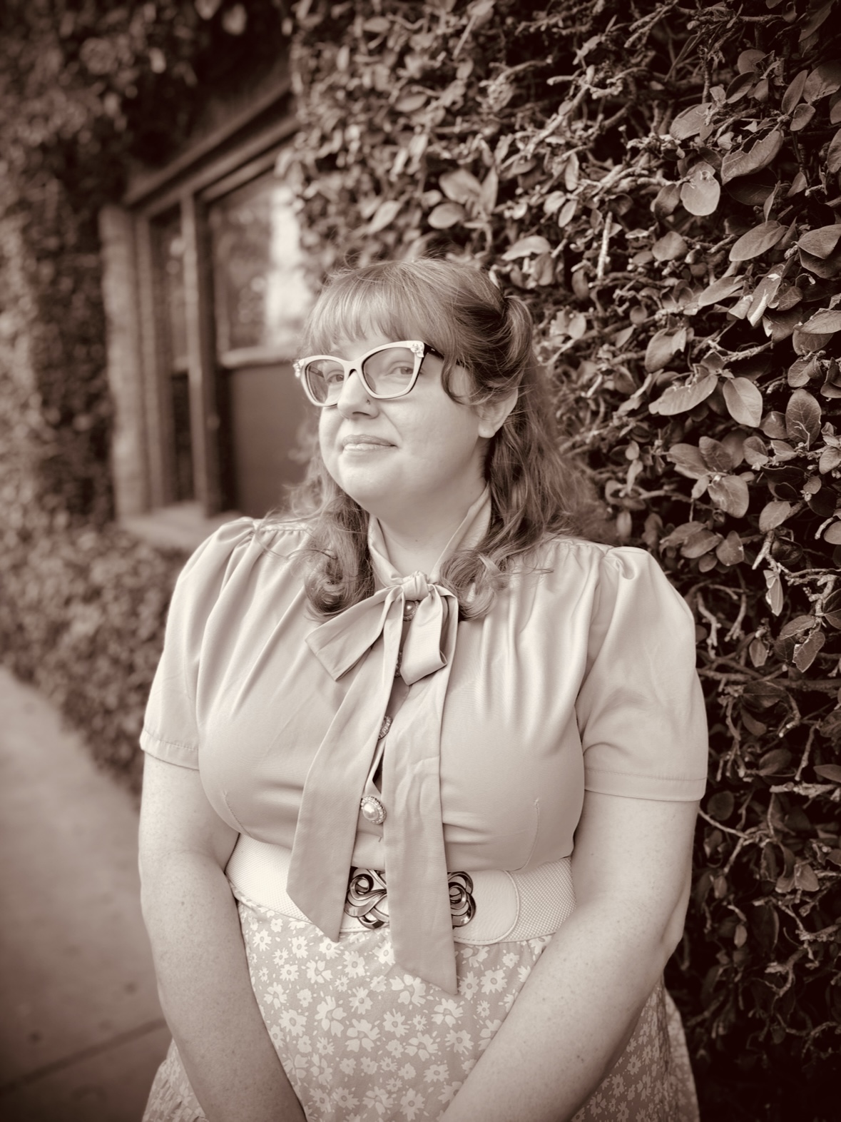 Sepia colored image of a blonde woman with glasses smirking at the camera.