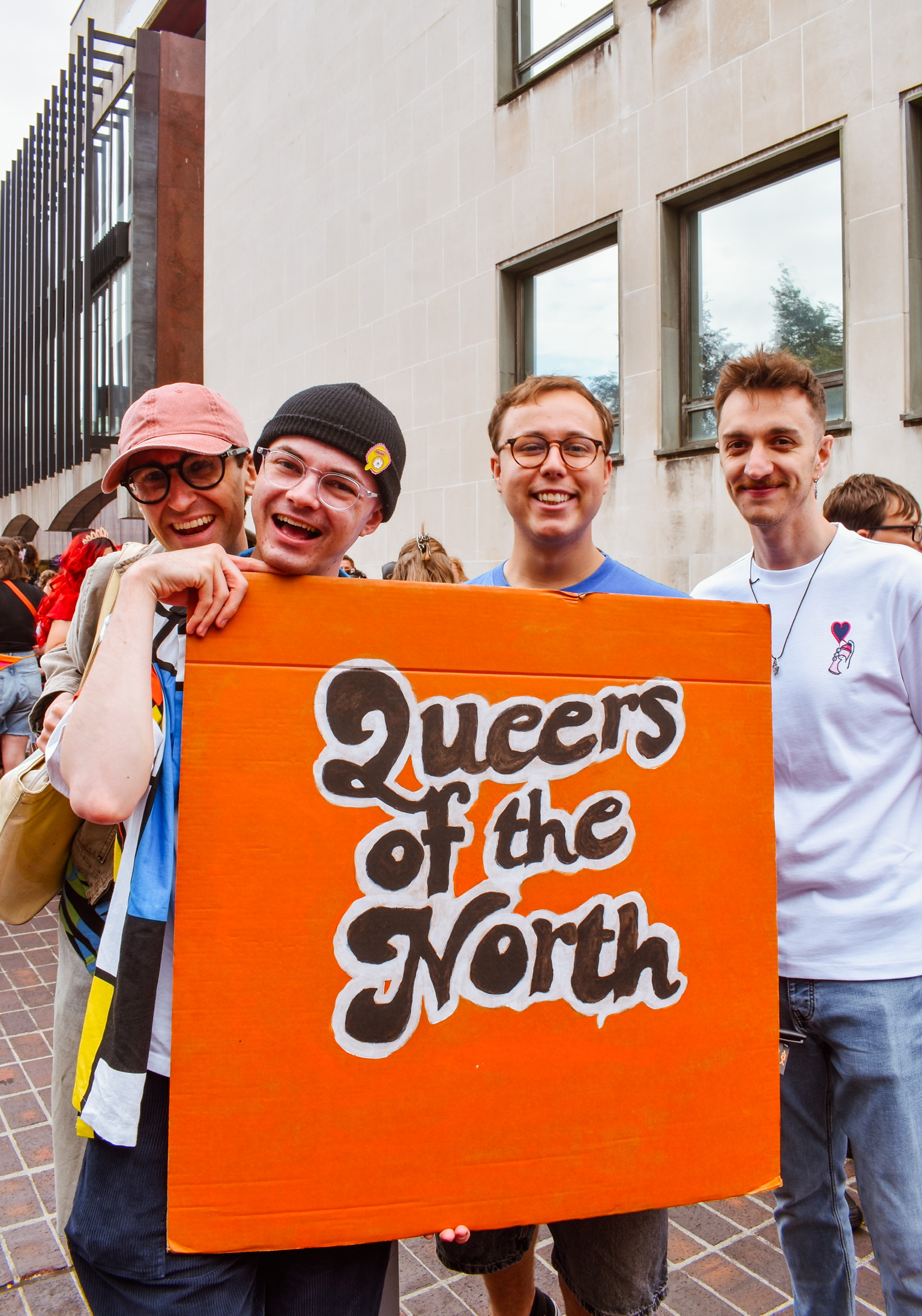 Four smiling Network members holding the hand-painted Queers of the North sign at Newcastle Pride