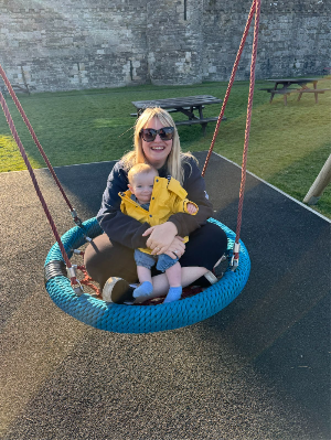 Georgina, a lady with blonde hair, sat a swing with a child in a yellow coat.