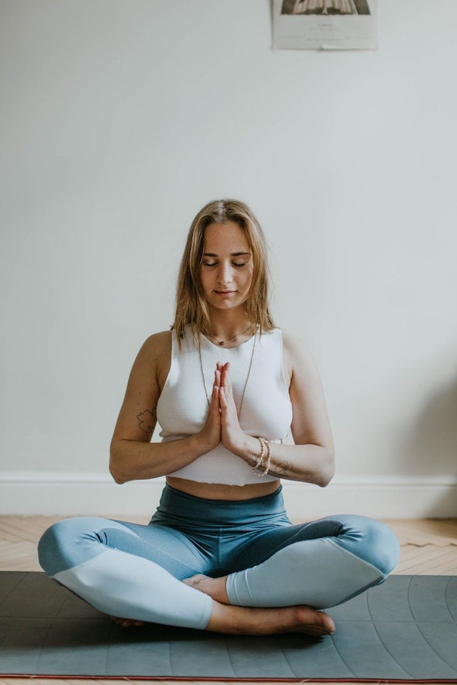 a woman in lotus position, eyes closed, hands in prayer, for guided meditation