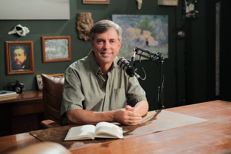 Dave Fleet seated at his desk beside a microphone and an open book