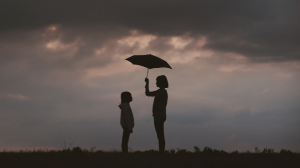 Junge Frau die einen Regenschirm über ein Kind hält