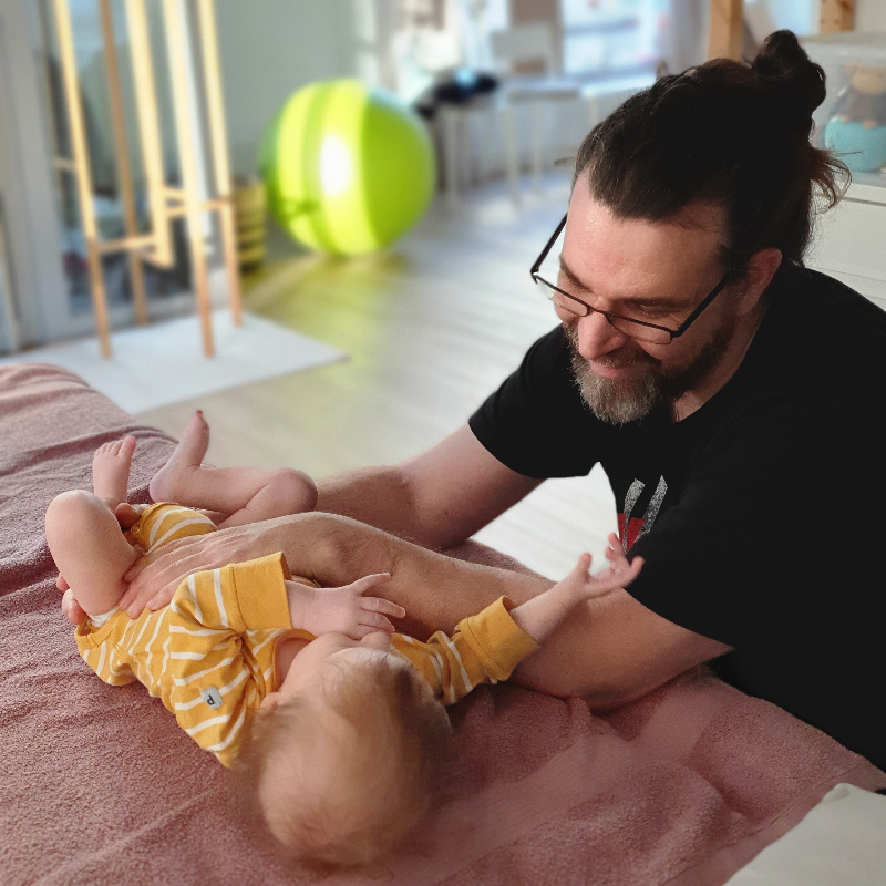 Osteopaatti Jari Kauppila pitelee käsillään hoitopöydällä hymyilevää vauvaa