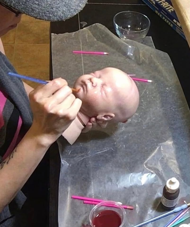 Jennifer at her worktable, blushing a doll's face