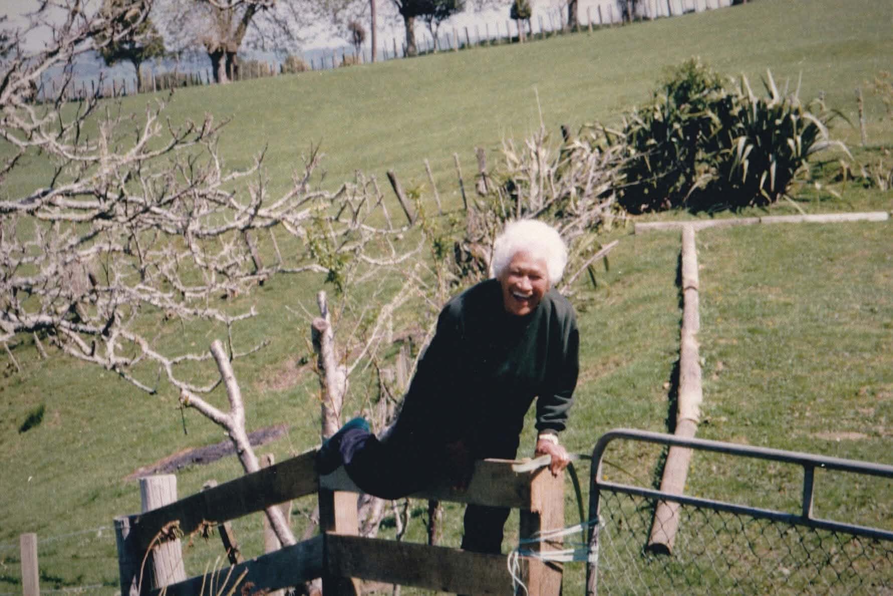 Nana Miriama Tahi at her homestead, with harakeke growing behind her