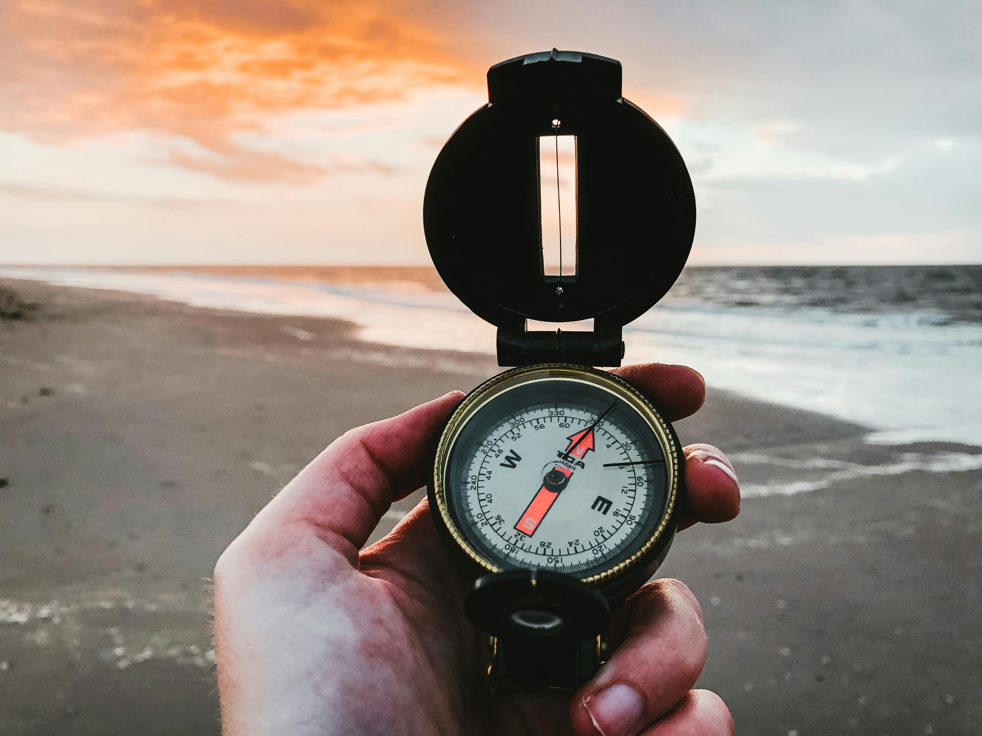 Hand holding a compass on a beach at sunset