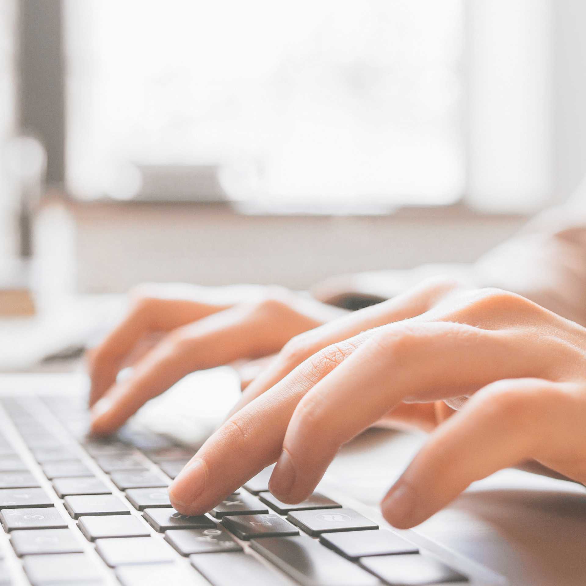 A closeup of the fingers of two hands, typing on the keyboards of a laptop.