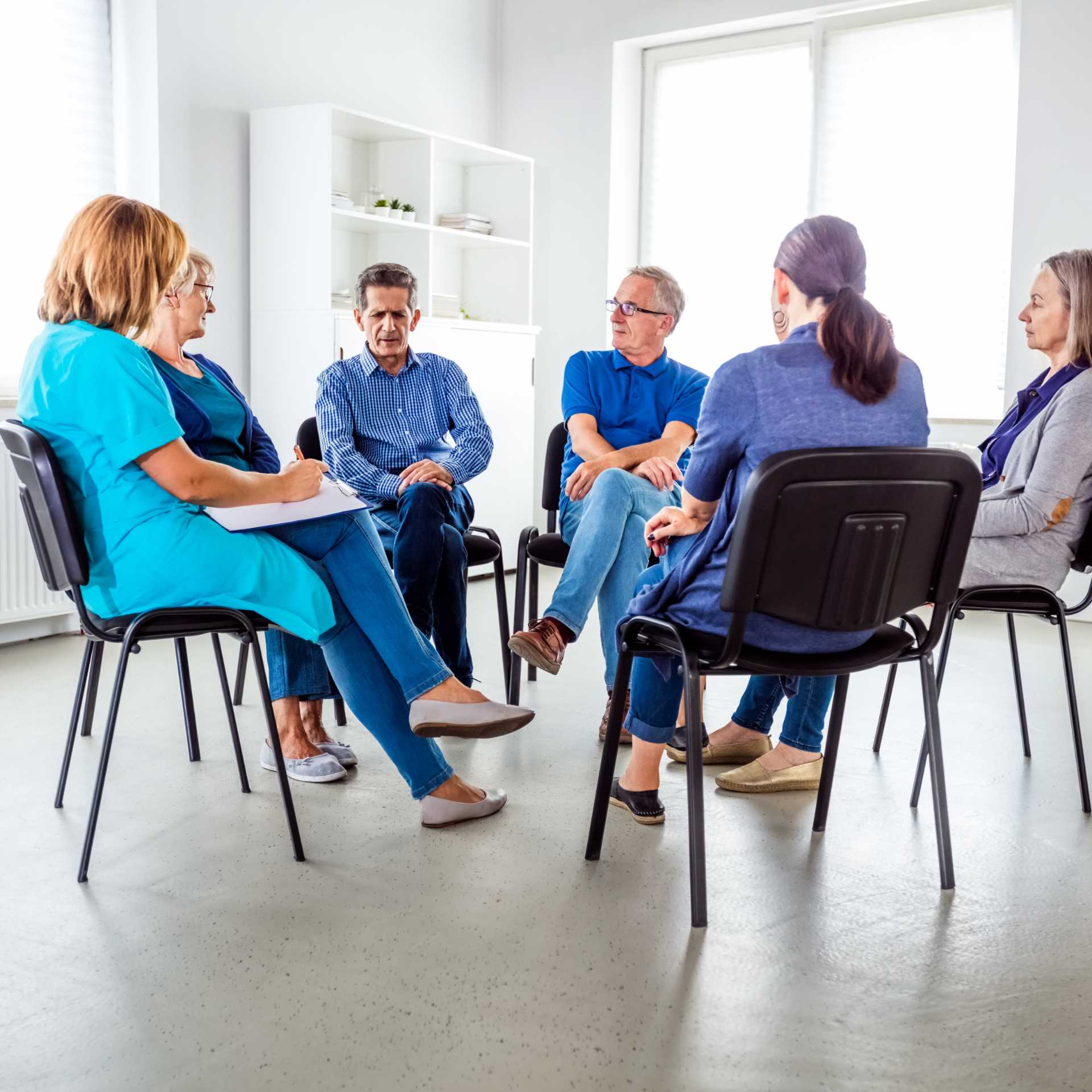 A group of people sitting on chairs in a circle, discussing.