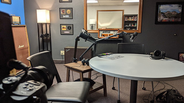 In The AV Department podcast studio is a table, two chairs, multiple cameras, two microphones on boom arms and professional lighting.