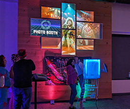 A mosaic of eight digital displays show a music video and text identifying the Photo Booth area.