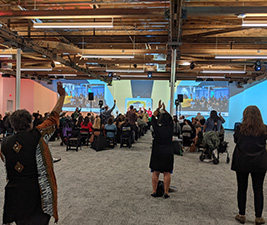 The in-person audience at a hybrid breakfast fundraiser wave to the cameras as the online audience tunes in to the event.