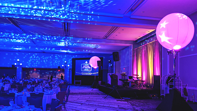 Upights and projected patters in white add a dynamic element to a ballroom bathed in blue lighting while magenta and gold uplights bring attention to the stage.