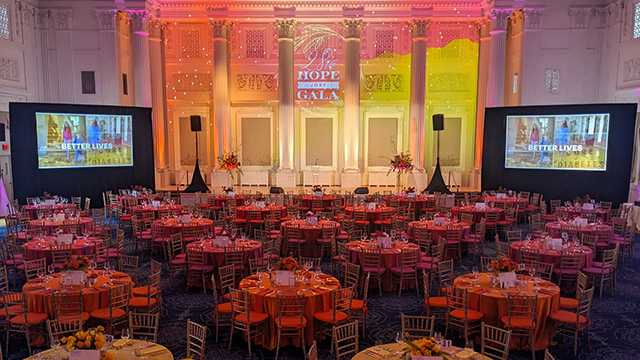 The gradient color shift from yellow to orange to red is seen in both the table linens and in the lighting and video projection in a ballroom set for a nonprofit gala.