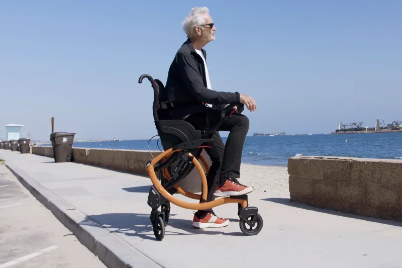 Homem em uma cadeira de rodas a beira mar, ele pode colocar os pés no chão graças ao modelo da cadeira Zeen